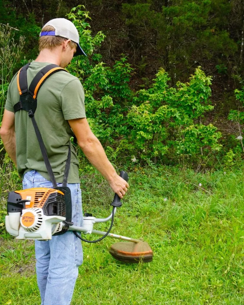 Crew member trimming grass and brush along a property edge.