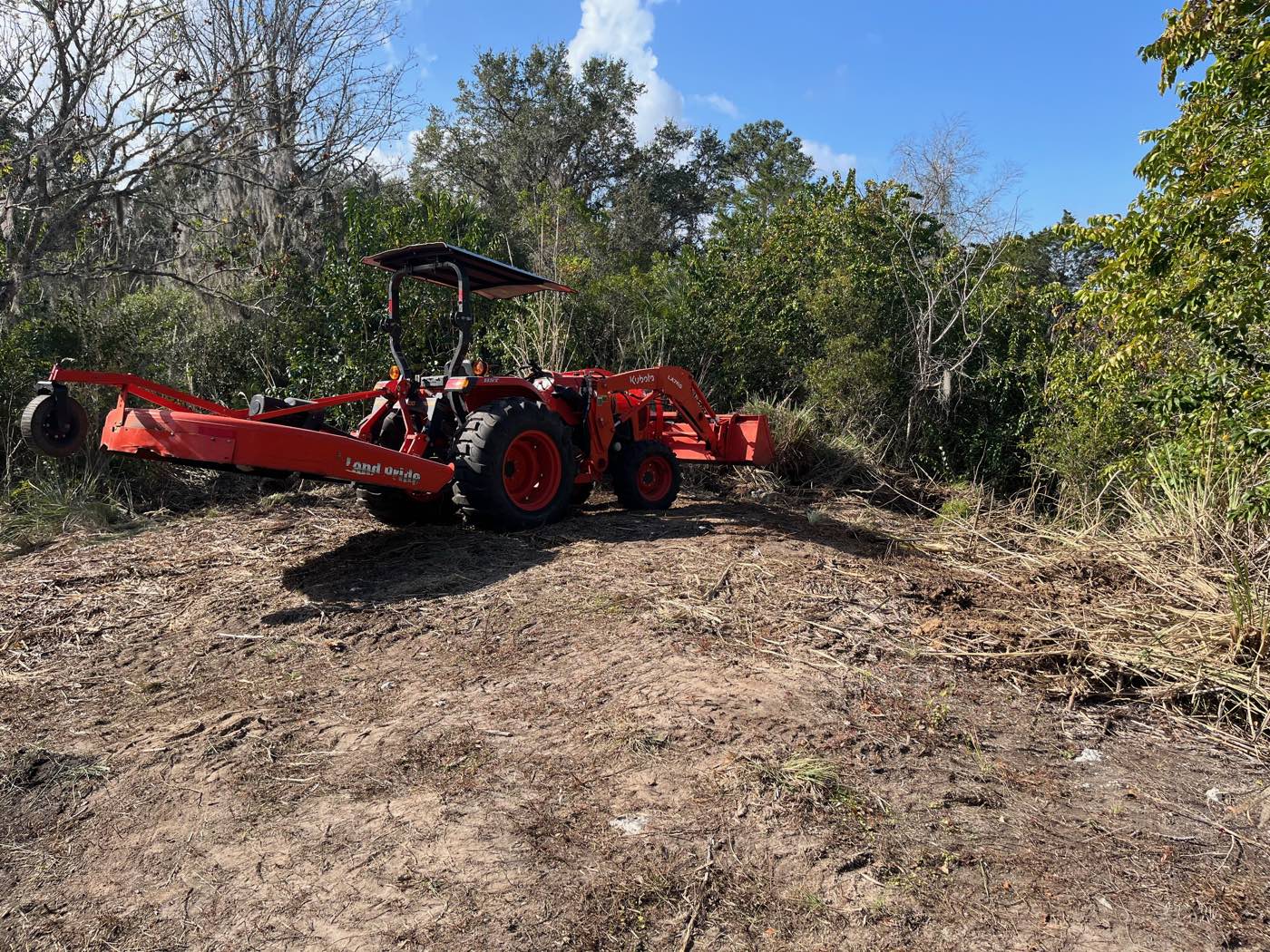 Kubota tractor and brush hog clearing an overgrown lot